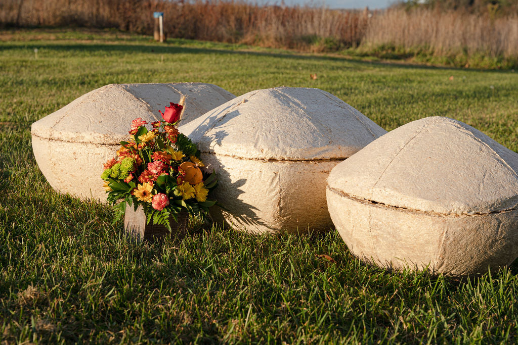 Three mushroom pet coffins on grass with a floral arrangement in front