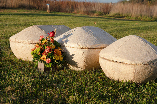 Three mushroom pet coffins on grass with a floral arrangement in front